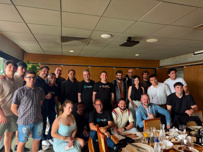 A large group of people pose together at a dinner table, with several individuals wearing shirts branded with the 'OneEx' logo.