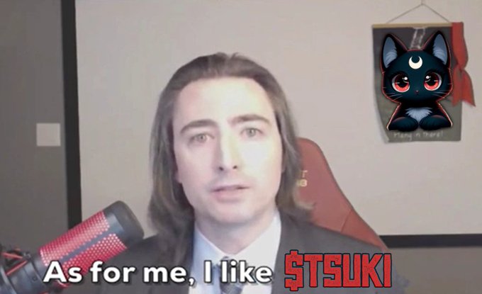 A long-haired man sits in front of a microphone in a room with a black cat tapestry on the wall, with on-screen text reading "As for me, I like $TSUKI" — referencing the crypto token highlighted in the accompanying post about Tsuki's mysterious timing connection to Roaring Kitty's 2024 return.