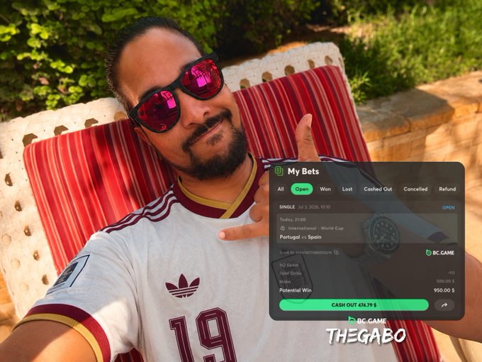 A man wearing sunglasses and a white and maroon Adidas jersey takes a selfie while lounging on a striped cushion outdoors, overlaid with a BC.Game "My Bets" interface showing an open $500 wager on the Portugal vs. Spain World Cup match with a potential $950 win, alongside "THEGABO" branding—visually reinforcing his post about betting on Spain in the 2026 World Cup Round of 16.
