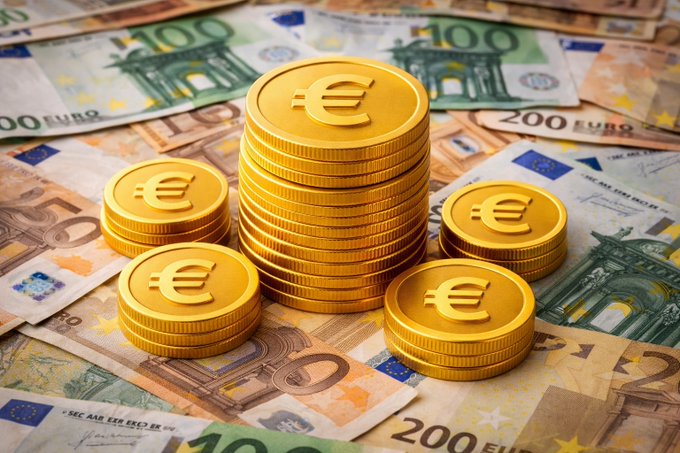 Stacks of gold Euro coins rest on a bed of Euro banknotes (€100 and €200 denominations), symbolizing European currency and financial regulation. The image visually reinforces the post about the European Commission reviewing the MiCA (Markets in Crypto-Assets) framework to address tokenized financial instruments and stablecoin models within the EU.
