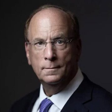 The image features a man wearing glasses, a suit, and a tie. He has a serious expression as he looks directly at the camera. The background appears to be black, which contrasts with his attire and accentuates him. There are no other objects or texts in the image, making it a simple yet impactful composition that highlights the subject's presence against the dark backdrop.