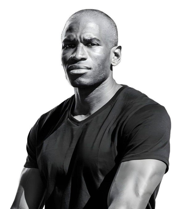 A muscular Black man in a black v-neck t-shirt is photographed against a white background, his expression serious and contemplative. The image accompanies a post about Arthur Hayes' "Yen-quake" essay predicting a Treasury-engineered weaker dollar and subsequent crypto rally, though no connection between the man pictured and the financial commentary is established.