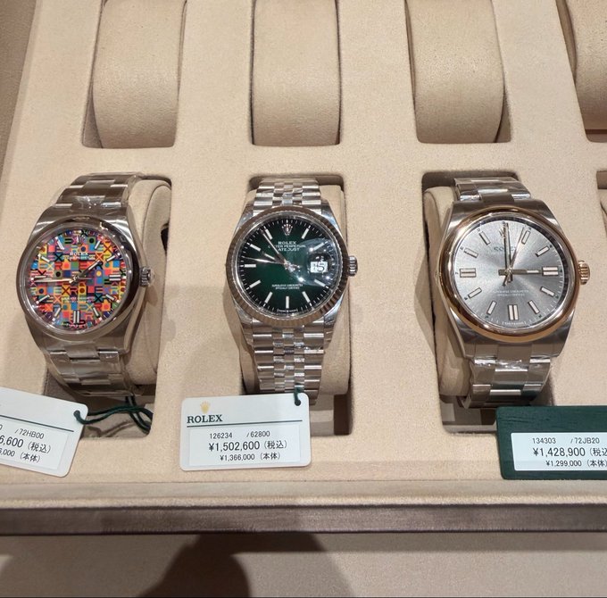 A display case showing three luxury Rolex watches with price tags in Japanese yen, including models 126334 (green dial) for ¥1,502,600 and 134303 for ¥1,428,900.