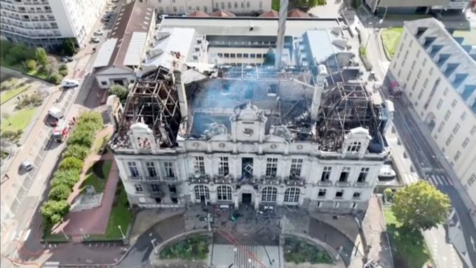 An aerial view of a large, ornate building that has suffered major damage to its roof, with the destroyed interior exposed to the sky.