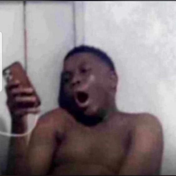 A shirtless young man holding a phone in front of his face, his mouth wide open in an exaggerated shocked or screaming expression.