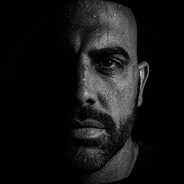 A black-and-white close-up portrait shows a bearded man with a shaved head and a serious expression, his face half-shadowed against a dark background. The accompanying post humorously compares his baldness to Coinbase CEO Brian Armstrong's, joking that both men will regrow their hair before Trump signs the CLARITY Act—a play on the well-known bald status of the Coinbase CEO, which has become a meme in crypto circles.