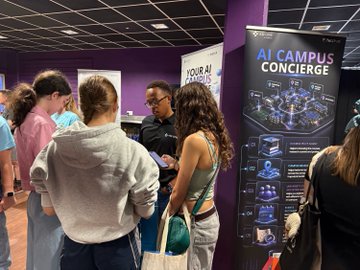 A group of people gather around a tall black display banner labeled 'AI CAMPUS CONCIERGE' featuring 'SMART NETWORKING' at what appears to be a technology or networking event.