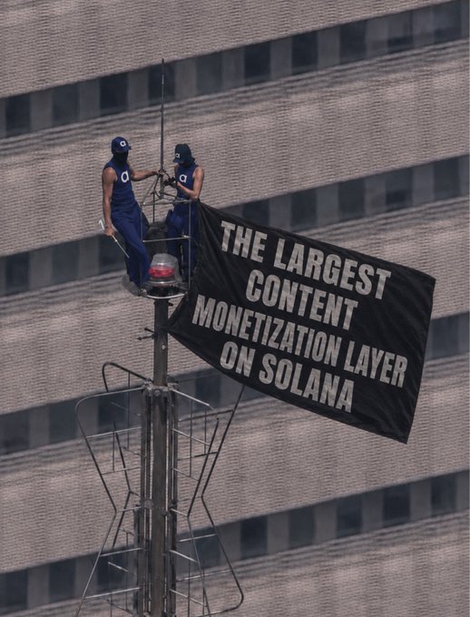 Two workers stand atop a tall structure holding a large black banner reading "THE LARGEST CONTENT MONETIZATION LAYER ON SOLANA," visually reinforcing Access Protocol's bold claim of being the premier content monetization platform on the Solana blockchain.