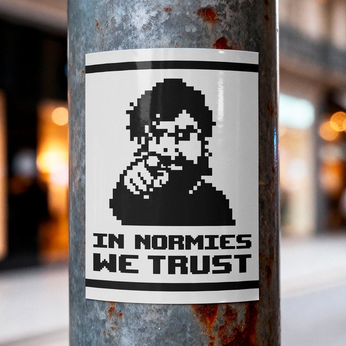 A black and white pixel-art style sticker on a metal pole depicting a hooded figure smoking, with the text 'IN NORMIES WE TRUST'.