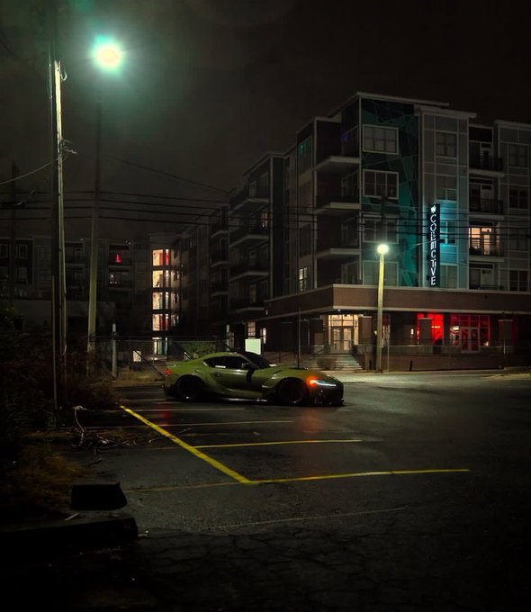 A green sports car parked at night in front of an apartment building illuminated by a green streetlight.