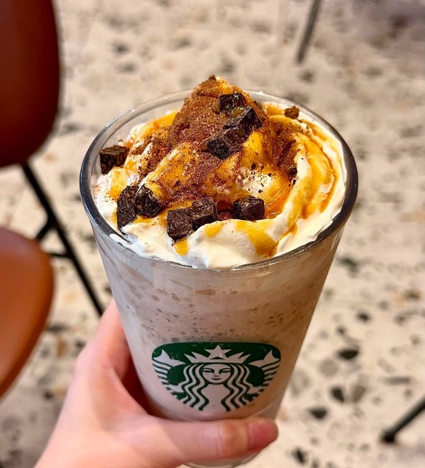 A hand holds a tall Starbucks frappuccino topped with whipped cream, caramel drizzle, chocolate chunks, and cinnamon powder. The image of the Starbucks drink seems unrelated to the text discussing cryptocurrency exchange regulations and trading deadlines in Vietnam.