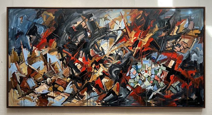 An abstract expressionist painting features chaotic brushstrokes in red, blue, black, white, and earth tones, displayed in a wooden frame on a white wall.