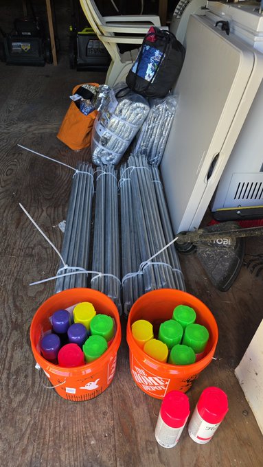 Construction supplies including metal rods, orange Home Depot buckets filled with colorful spray paint cans, and other equipment sit on a wooden floor.
