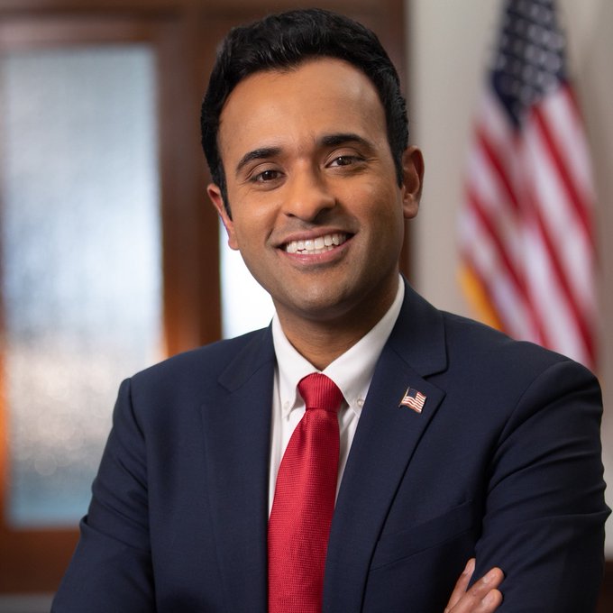 A professional headshot of Vivek Ramaswamy, founder of Strive Asset Management, wearing a navy blue suit with a red tie and an American flag lapel pin, smiling with an American flag visible in the background. The image accompanies news of his company Strive's $37 million Bitcoin acquisition of 469 BTC, contributing to their growing holdings of 25,000 BTC.