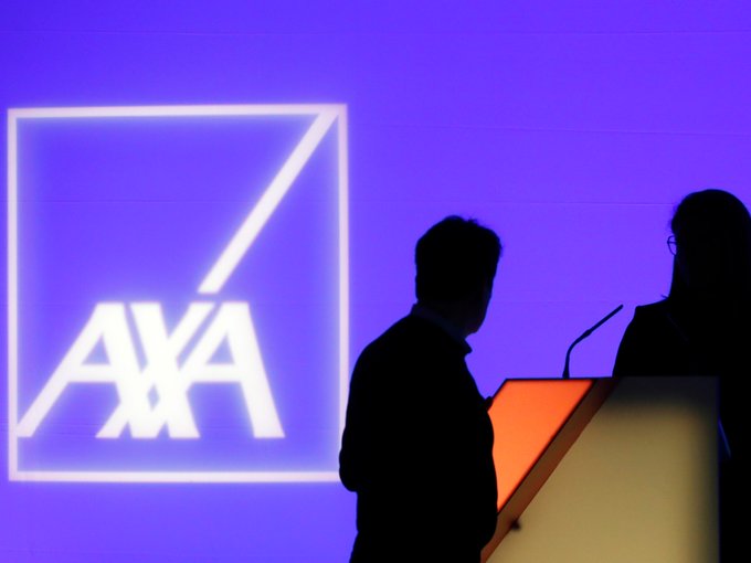 A photograph of silhouetted speakers at a podium during a corporate event, with a large illuminated 'AXA' logo displayed on a screen behind them against a blue background.