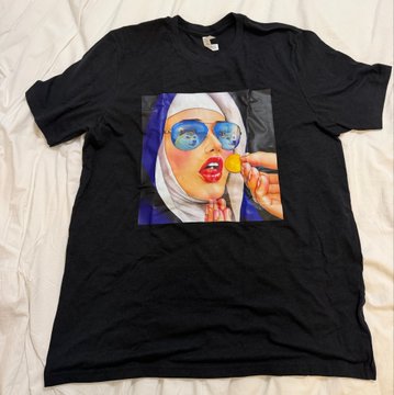 A black t-shirt featuring a vibrant graphic print of a woman wearing a hijab and sunglasses, holding a yellow lollipop.