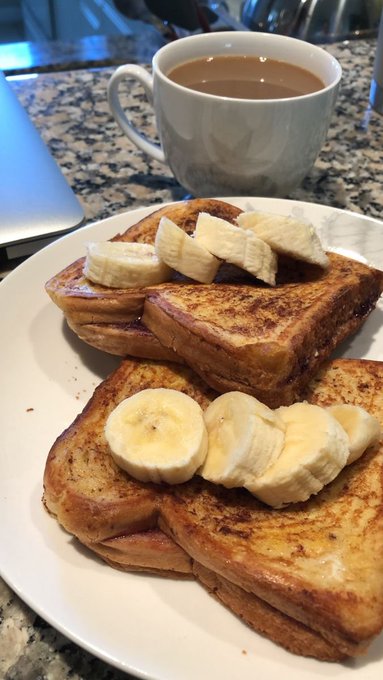 A plate of French toast topped with sliced bananas sits on a granite countertop next to a gray mug of coffee with milk.