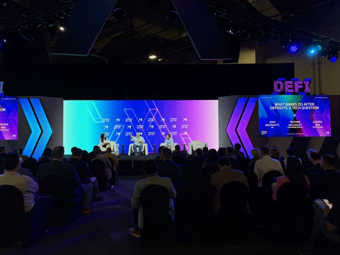 A Money2020 USA panel discussion takes place onstage before a seated audience, with “DEFI” branding and a screen asking, “WHAT BANKS DO AFTER DEPOSITS: A TECH QUESTION.” The session features Louis Bai of Anchorage, along with Nathan McCauley of Anchorage and Reginaatto of m0, discussing stablecoins, tokenized deposits, and the role of banks when AI agents move money.