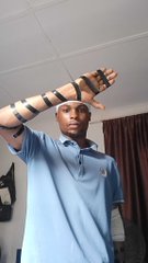 A young man wearing a light blue polo shirt and fingerless gloves posing with his arm crossed over his face in an indoor setting.