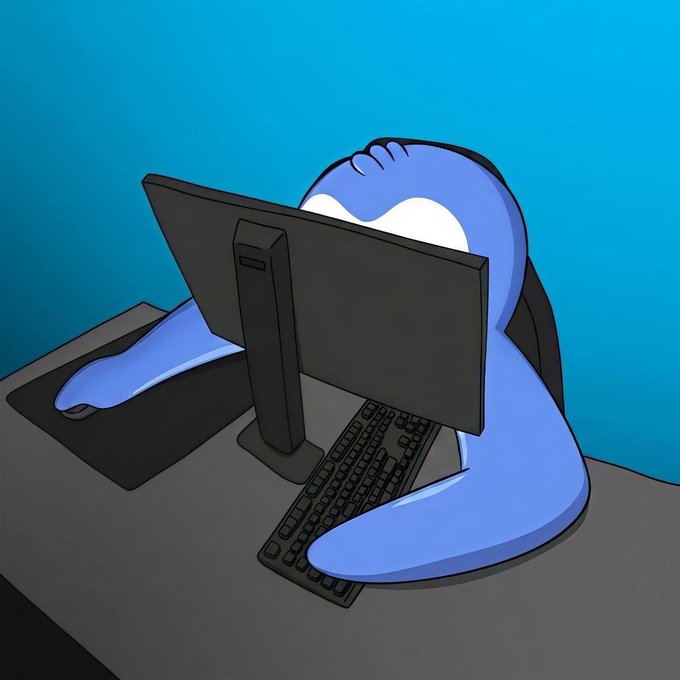 A blue cartoon creature with large white eyes sitting at a desk, using a computer monitor and keyboard, with its hands on a mouse.