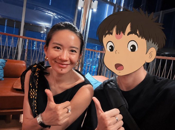 The image features a woman wearing a black dress, posing with a man who has a cartoon character face drawn over his shoulder. The woman is giving a thumbs up gesture while they are both smiling for the camera. The caption of the image reads "What One is my favorite female KOL in the crypto circle Everyone can follow her more @heyibinance".