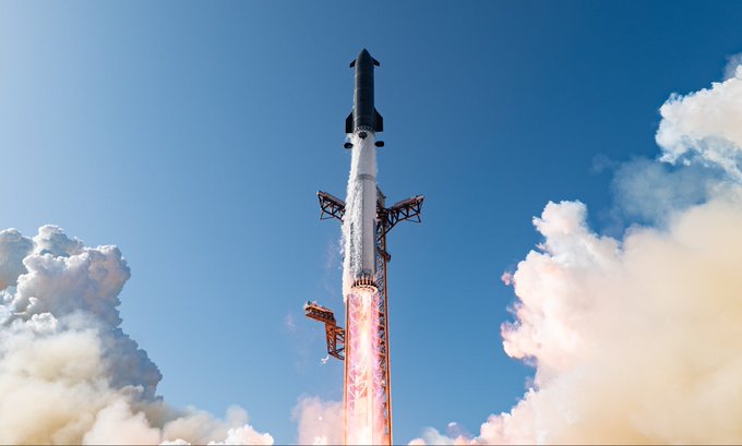 A rocket launches into a blue sky, ascending with flames and smoke billowing from its engines as it passes launch tower structures.