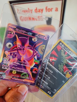 A hand proudly displays two Japanese Pokémon trading cards, including a vibrant Holo card labeled "ブースター" (Booster) with "230" and what appears to be a Gyarados card numbered "297," captured right after a fun pack-opening session with the user's son. The handwritten note in the background reads "lucky day for a GUINNESS," adding a cheerful, personal touch to the celebration of the exciting card finds.