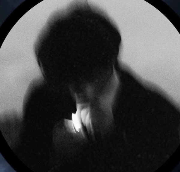 A grainy, dark black and white photo of a person lighting a cigarette from a lighter.