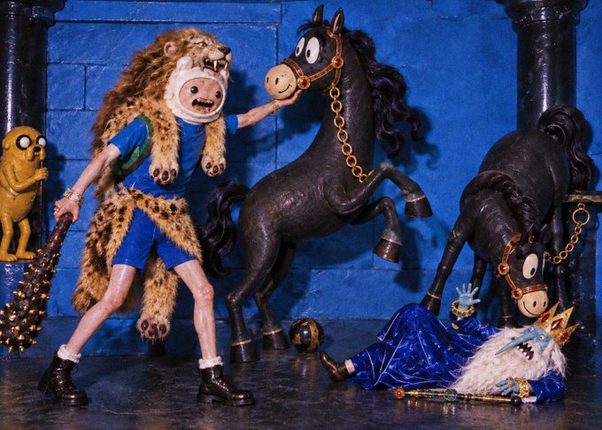 A figurine of a person in a leopard headdress and blue outfit stands next to a black toy horse and a small yellow dog, while another figure in blue robes lies on the ground.