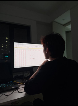 A person works late at night in front of a computer monitor displaying what appears to be a spreadsheet with trading data, with a keyboard illuminated by a backlit glow on the desk. The image visually represents the trader mentioned in the post who uses a Kalman filter to run 7,437 predictions on Polymarket's crypto "up or down" markets, earning $10,418 over 20 days with a 54% win rate.