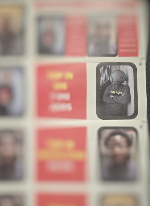 A close-up photo of a 'SHOP IN MY HOUSE SERIES' poster or display, with a small picture of a person in a gray Verizon hoodie and green headphones visible on the right side.