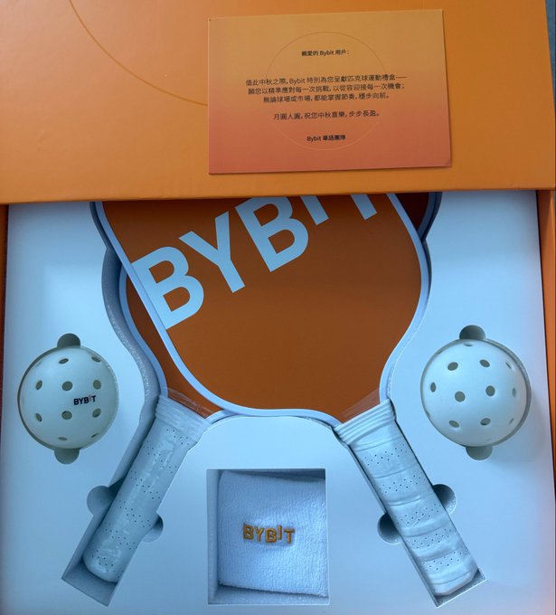 A Bybit branded gift box containing two pickleball paddles, two wiffle balls, and a wristband, with an orange card thanking the user in Chinese.