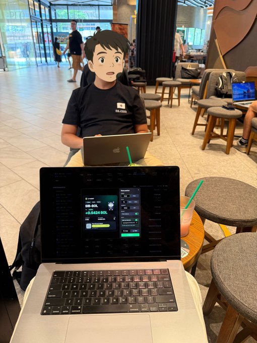 A person works on a laptop displaying crypto trading interfaces showing BB-SOL and SOL values, seated in a cafe or lobby with another person using a laptop behind them.