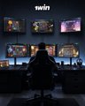A dark gaming or streaming setup featuring multiple monitors displaying game footage and colorful screens, with a gaming chair in the foreground and the text 'twitch' at the top.