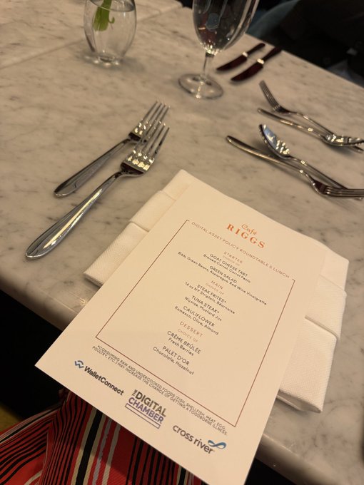 A marble dining table set with silverware, wine glasses, and a 'Café Riggs' menu for a 'Digital Asset Policy Roundtable Lunch' sponsored by WalletConnect, Digital Chamber, and Cross River.