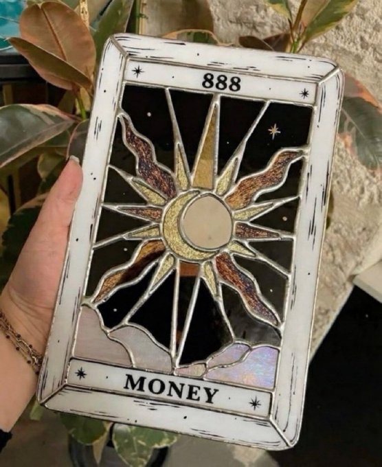 A hand holding a decorative stained-glass style card featuring a sun and moon design, labeled '888' at the top and 'MONEY' at the bottom.