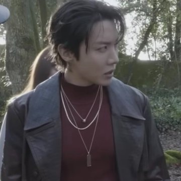 A young man with dark hair, wearing a burgundy shirt and leather jacket with layered necklaces, stands outdoors looking to the side. The caption "shibaaaaaaaaaal" suggests an enthusiastic exclamation, possibly referencing the Japanese dog breed Shiba Inu, though no dog is visible in the image.