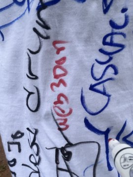 A white t-shirt with handwritten signatures and text in red, blue, and black markers, including the word 'CASCADE' and what appears to be 'Bob' and 'De'.