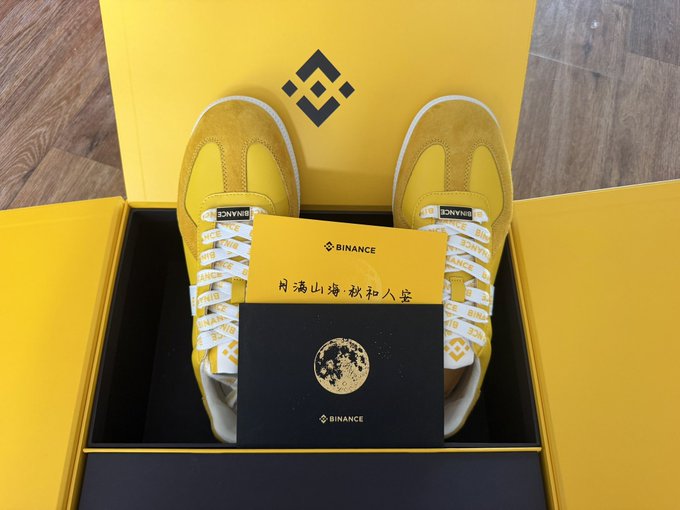 A pair of yellow Binance-branded sneakers displayed in a yellow Binance gift box, accompanied by a Binance card/envelope with a moon design and Chinese characters reading '月满山海 秋扣人堂'.
