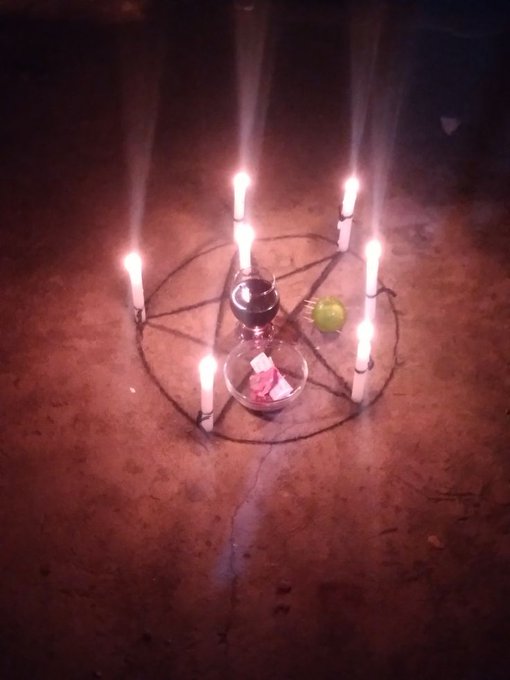 The image features a dark room with a large circle of candles arranged around a pentagram, which is a symbol often associated with magic and divination. The candles are lit, casting a warm glow throughout the space. In addition to the candles, there's an apple placed on top of the pentagram, possibly as a symbol or offering for the spell being performed. A bowl can also be seen in the room, which might contain items used during the ritual. The post about someone stealing from a wallet is unrelated to this image and does not provide any context or information that would help us understand how it connects with the scene depicted in the photo.
