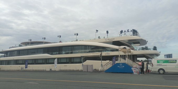 A large modern multi-deck riverboat or floating venue named "Elite" docked under a cloudy sky, with a white van parked nearby.