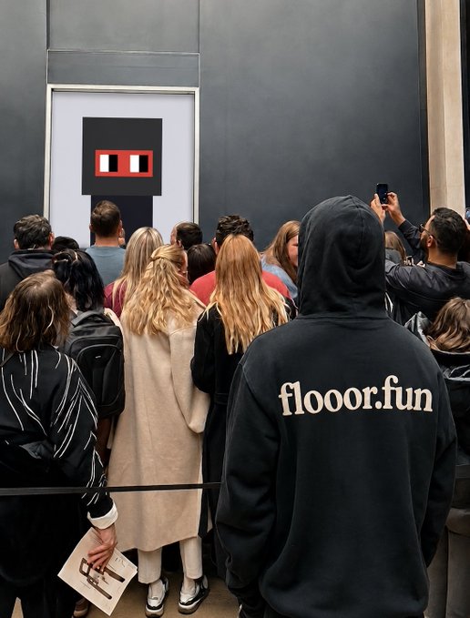 A crowd of people viewed from behind, with one person wearing a black hoodie reading 'flooor.fun', gathering in front of an artwork featuring a red rectangle on a black background.
