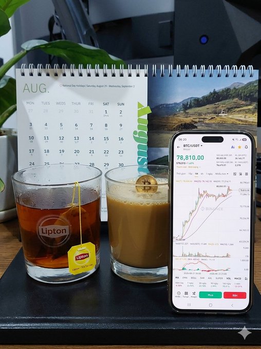 A desk scene with a Lipton tea glass and iced coffee next to a calendar, with a smartphone showing BTC/USDT chart at $78,810.00.