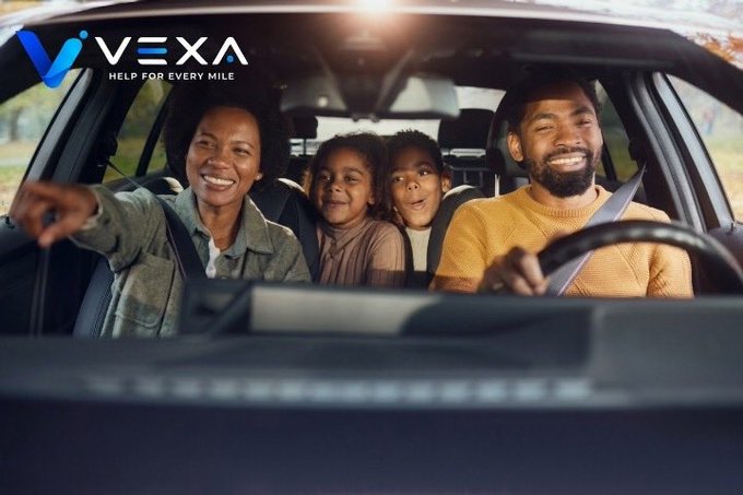 A smiling family of four enjoys a car ride together, with the "VEXA" logo and tagline "HELP FOR EVERY MILE" displayed in the upper left corner. The image aligns with the post by showcasing a happy, worry-free family road trip, reinforcing Vexa's mission to ensure smooth journeys without the stress of breakdowns.