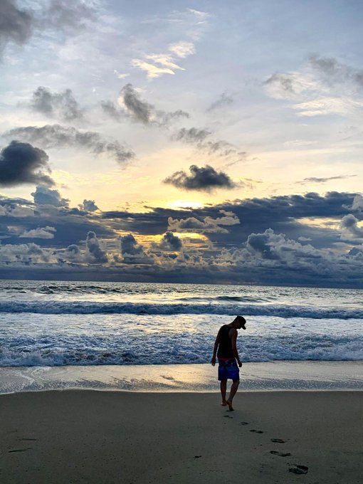 urn of water, dark blue sky with clouds, and a person walking on the beach at sunset.