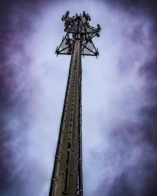A cell tower photographed from below against a dramatic purple-tinged cloudy sky.