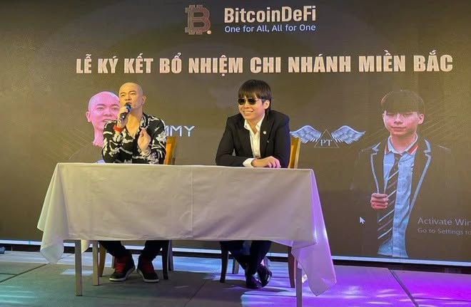 Two men sit at a table during a signing ceremony for 'BitcoinDeFi' Northern Branch in Vietnam, with Vietnamese text reading 'LỄ KÝ KẾT BỔ NHIỆM CHI NHÁNH MIỀN BẮC' on the backdrop.