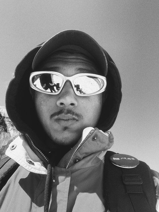 A black-and-white close-up portrait shows a man wearing a hood and reflective sunglasses, with snowy mountain reflections visible in the lenses.