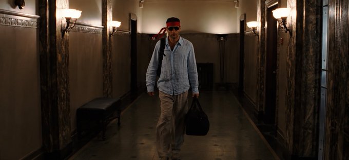 A man wearing a red headband walks confidently down a dimly lit, marble hallway carrying a duffel bag. The image evokes the determined, solitary spirit referenced in the $RKC post, suggesting a bold individual pursuing financial opportunity on their own terms.