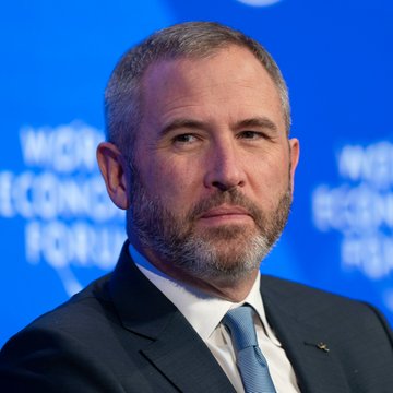 A man in a dark suit with a blue tie appears at the World Economic Forum, with the event's branding visible on the blue backdrop behind him. The image accompanies news about Ripple CEO Brad Garlinghouse expressing optimism despite the CLARITY Act's failed cloture vote.